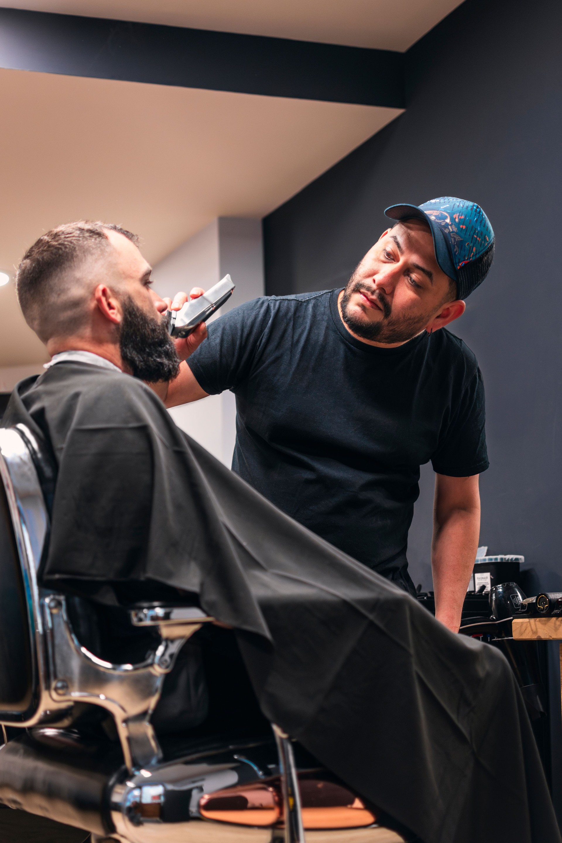 A man is having his beard trimmed with an electric razor. The man is sitting in an old barber's chair.