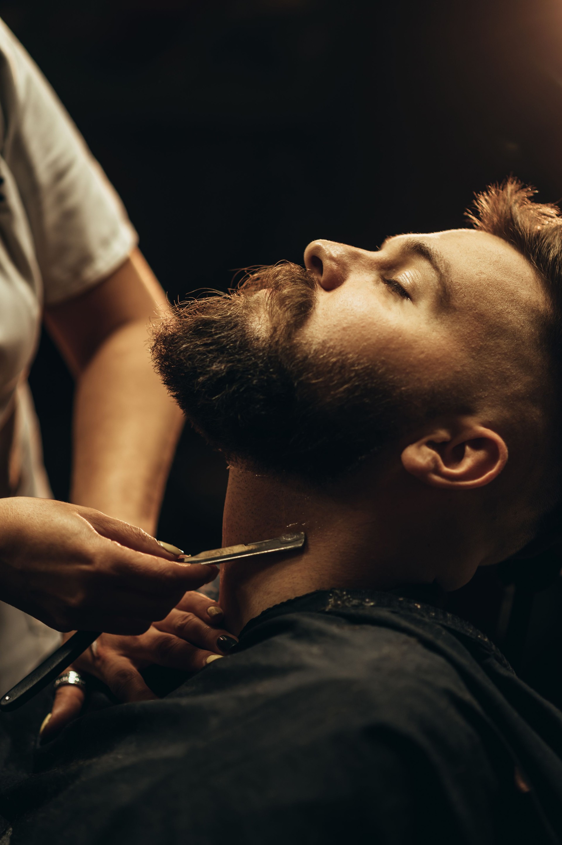 Man getting shaved with straight edge razor by hairdresser at barbershop